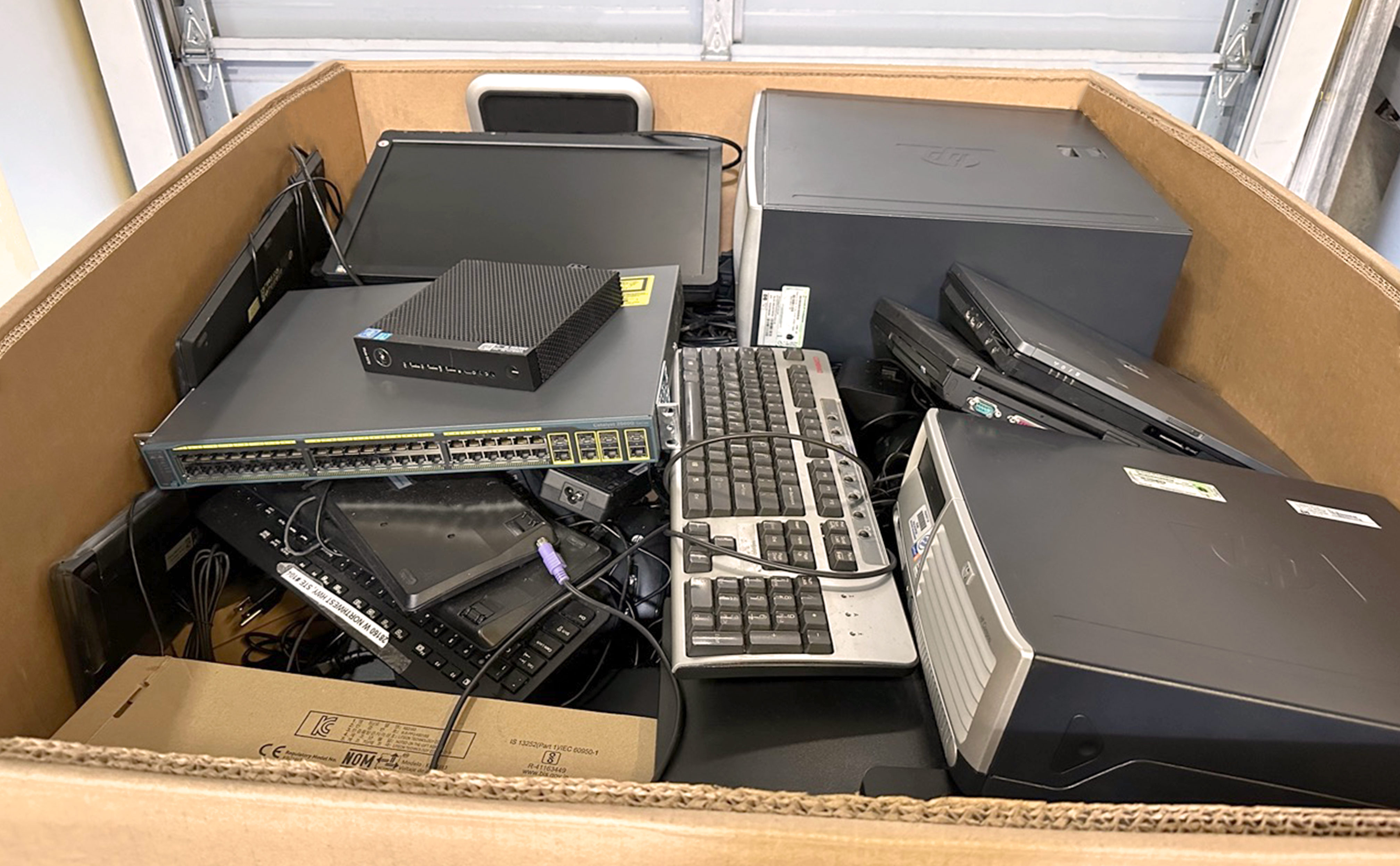 800 pound electronics recycle box detail view - open top box fully loaded with a large variety of office electronics sitting near a closed garage door