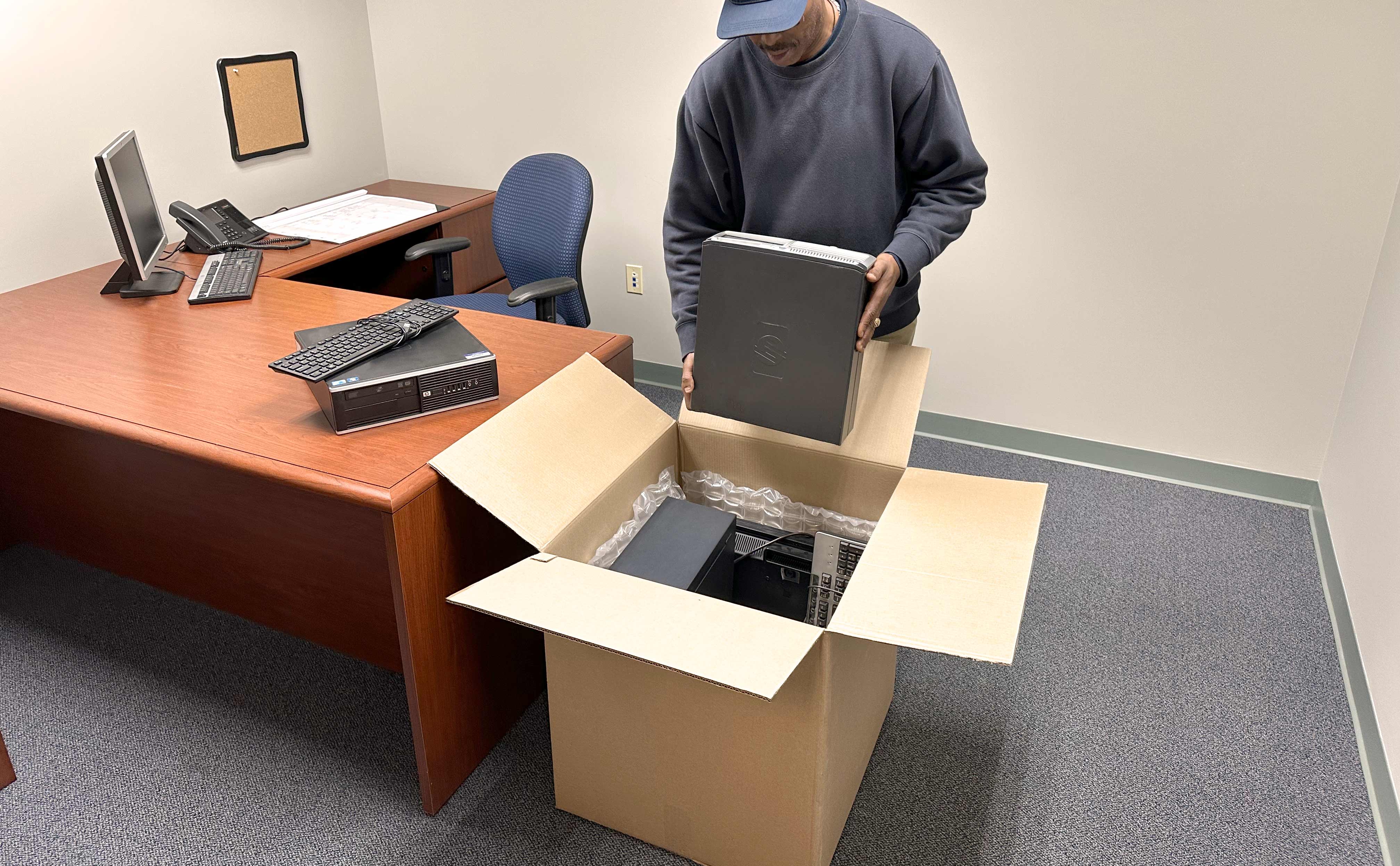 70 pound electronics recycle box on office room floor - man placing computer in box amongst a variety of office electronics